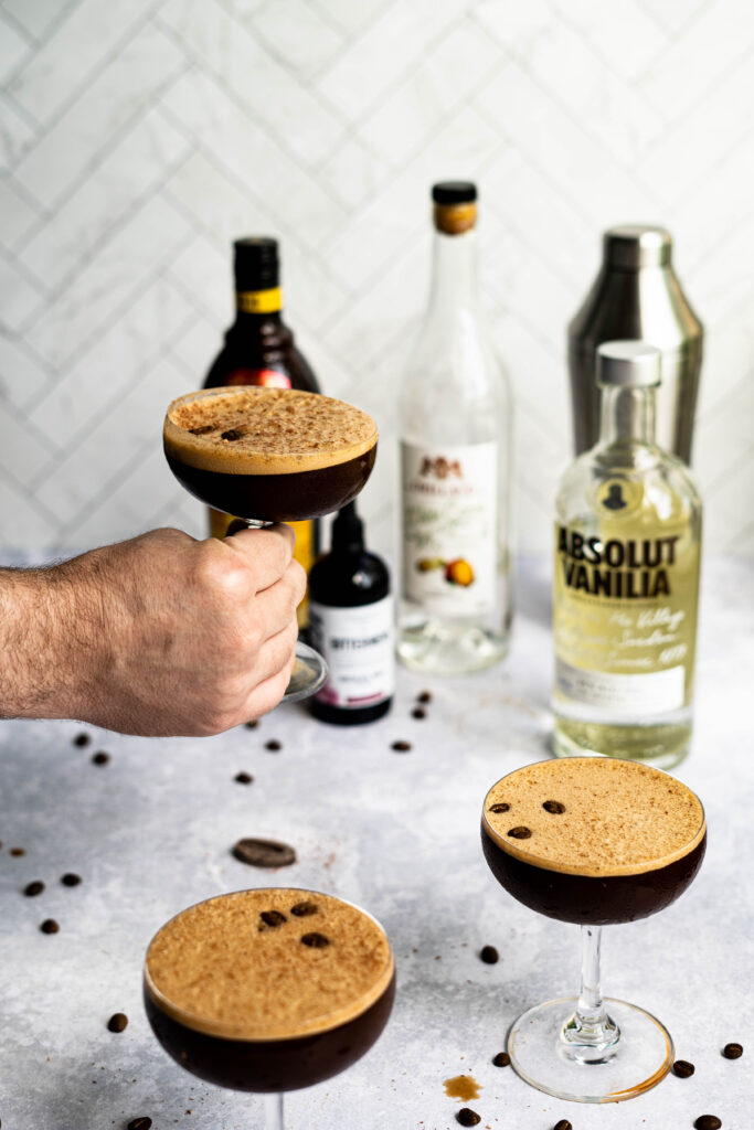 A hand from out of frame is grabbing a Chocolate Espresso Martini from a countertop. The photo was taken by Orlando Drink Photographer, Lindsey Neumayer.