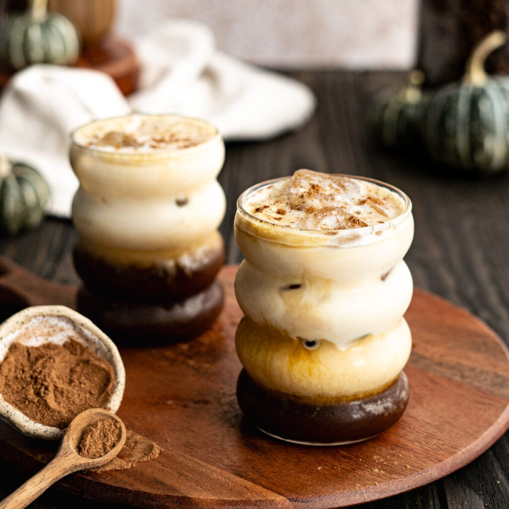 A photograph shows two pumpkin spice shaken espressos on a wooden cutting board, with a spoonful of pumpkin spice in the foreground. The photo is taken by Central Florida Food and Beverage Photographer, Lindsey Neumayer.